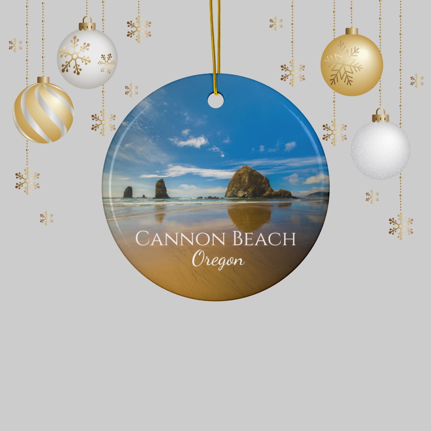 Round ornament with Cannon Beach, Oregon scene surrounded by Christmas ornaments on a light gray background