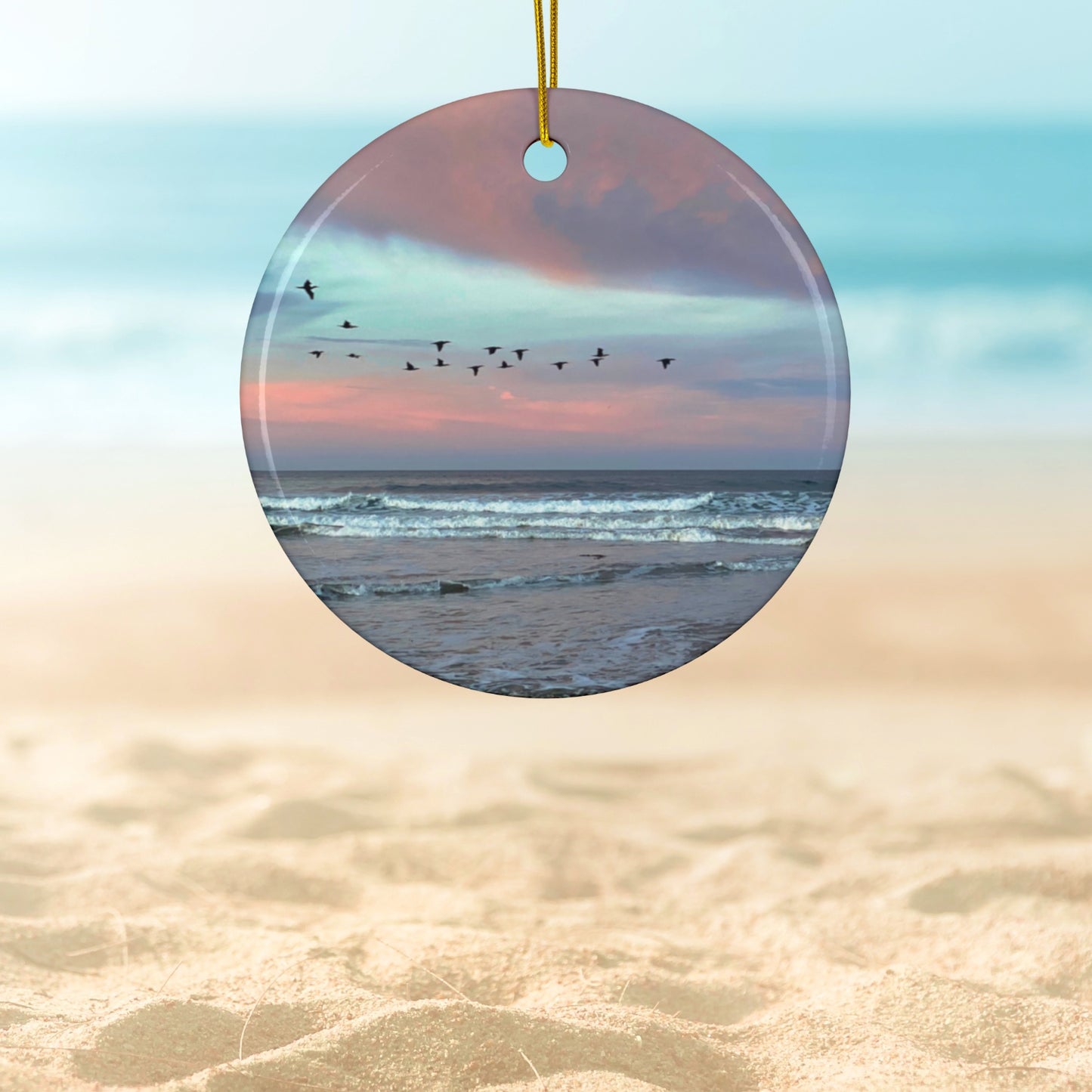 Ceramic holiday ornament featuring a photograph of a flock of birds flying across a pastel pink and violet sunrise sky over the Pacific ocean.
