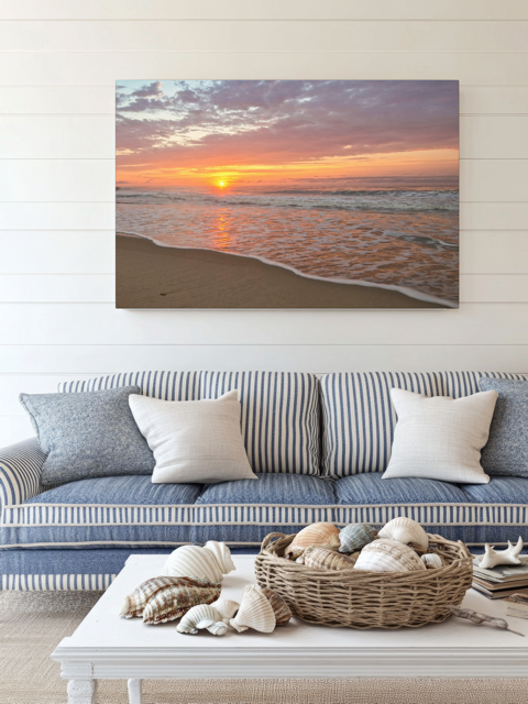 Canvas print of a vibrant sunrise over the Atlantic Ocean above a striped sofa with decorative items on a coffee table.