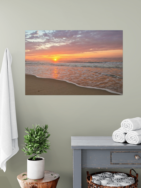 Canvas print of a vibrant sunrise over the Atlantic Ocean on a wall above a table with a plant and folded towels.