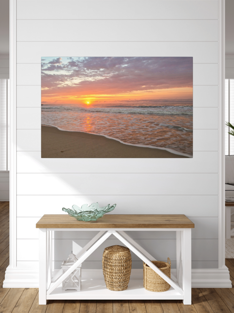 Canvas print of a vibrant sunrise over the Atlantic Ocean on a wall above a wooden bench with storage.