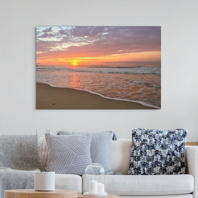 Canvas print of a vibrant sunrise over the Atlantic Ocean above a sofa with decorative pillows