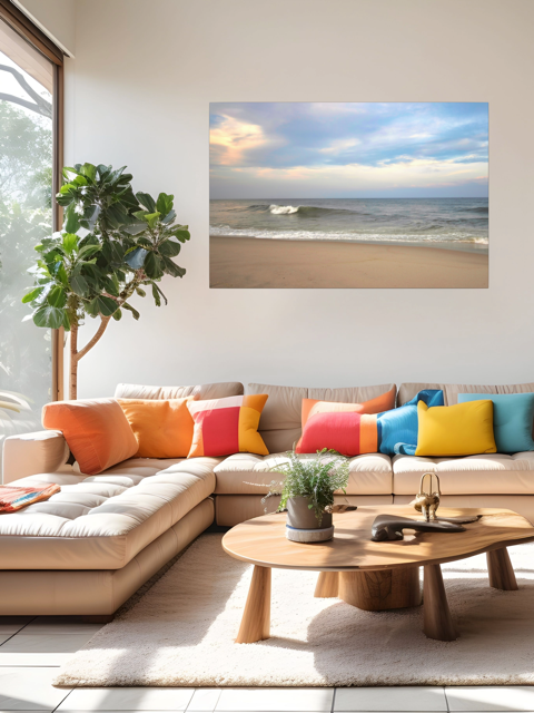 Modern living room with a sectional sofa, colorful pillows, and a canvas print of a peaceful view of tiered ocean waves rolling on to a sandy beach under a soft peach and blue cloud-filled sky on the wall.