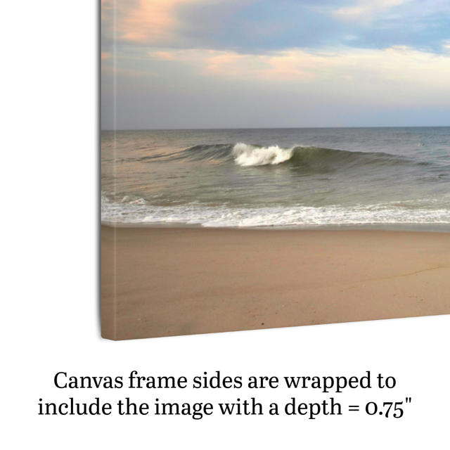 Side view of a canvas print of a peaceful view of tiered ocean waves rolling on to a sandy beach under a soft peach and blue cloud-filled sky showing the frame depth..