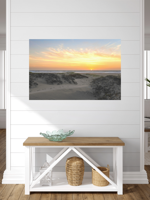 A canvas print of a beach dunes sunset on a white wall above a wooden bench with storage.