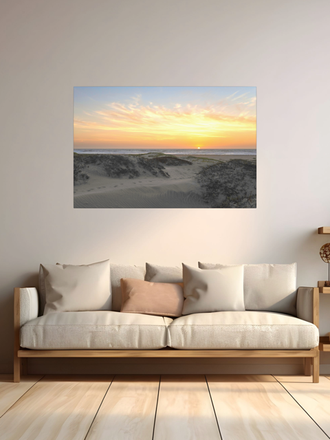 A canvas print of a beach dunes sunset on a wall above a sofa with cushions.