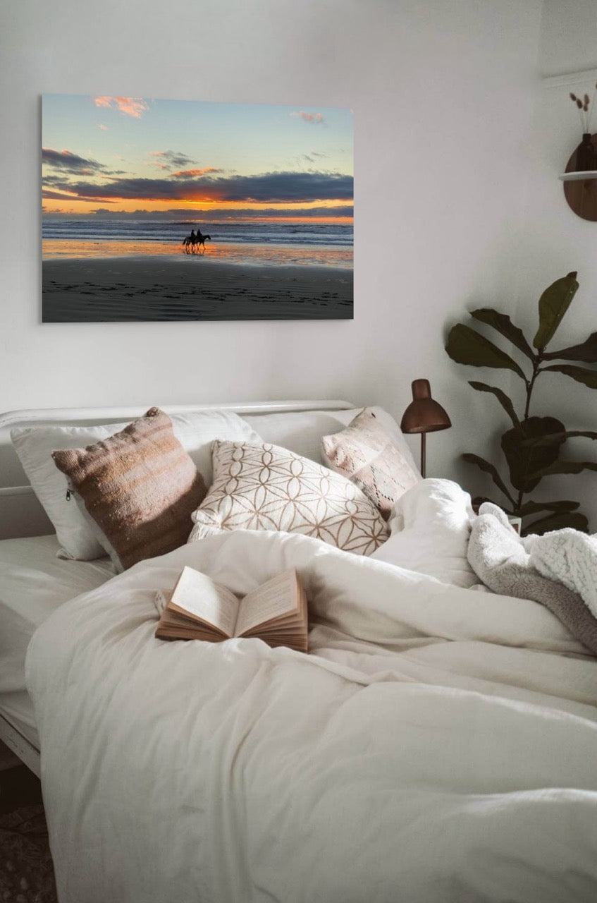 Bedroom with a canvas print of two horseback riders on the beach at sunset on the wall.