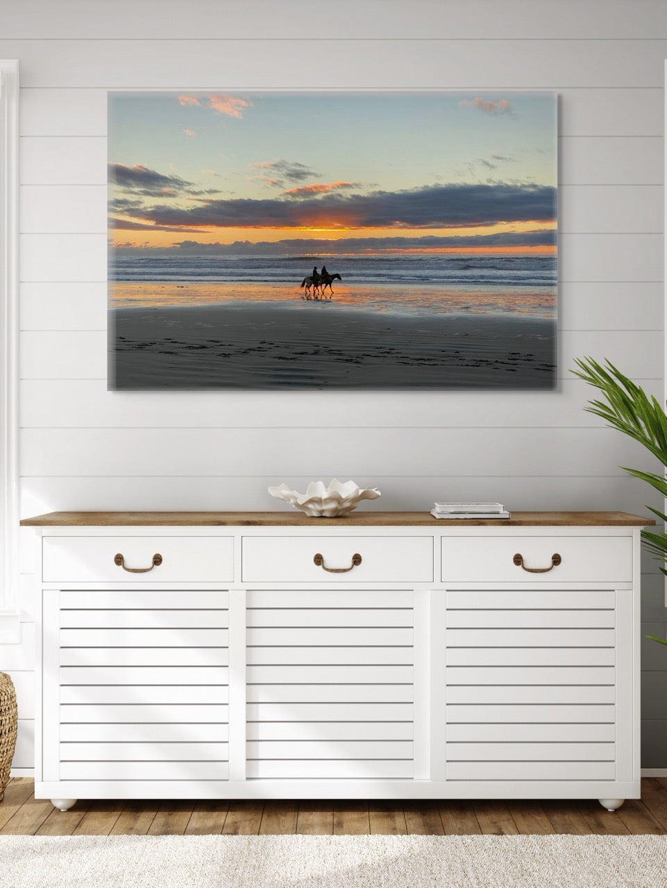 A canvas print of two horseback riders on the beach at sunset above a white cabinet with wooden top