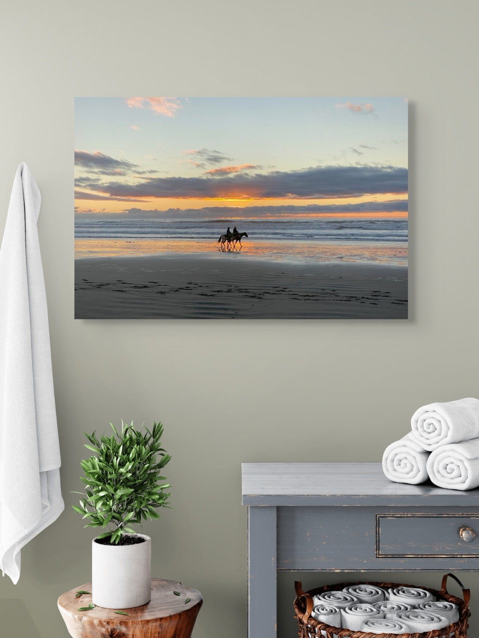 Canvas print of a beach scene with horses at sunset hanging on a wall above a dresser.