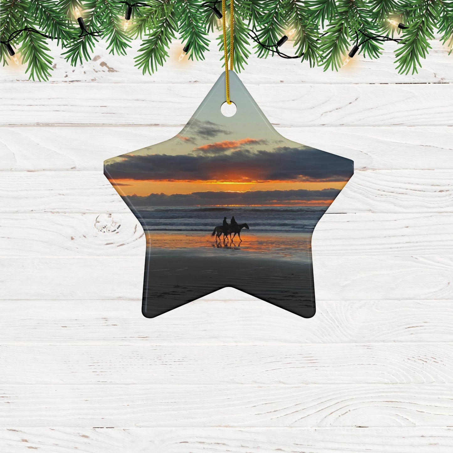 Star-shaped ceramic holiday ornament featuring a photograph of two horseback riders silhouetted on a beach at sunset with reflections in the wet sand, hanging from Christmas tree.