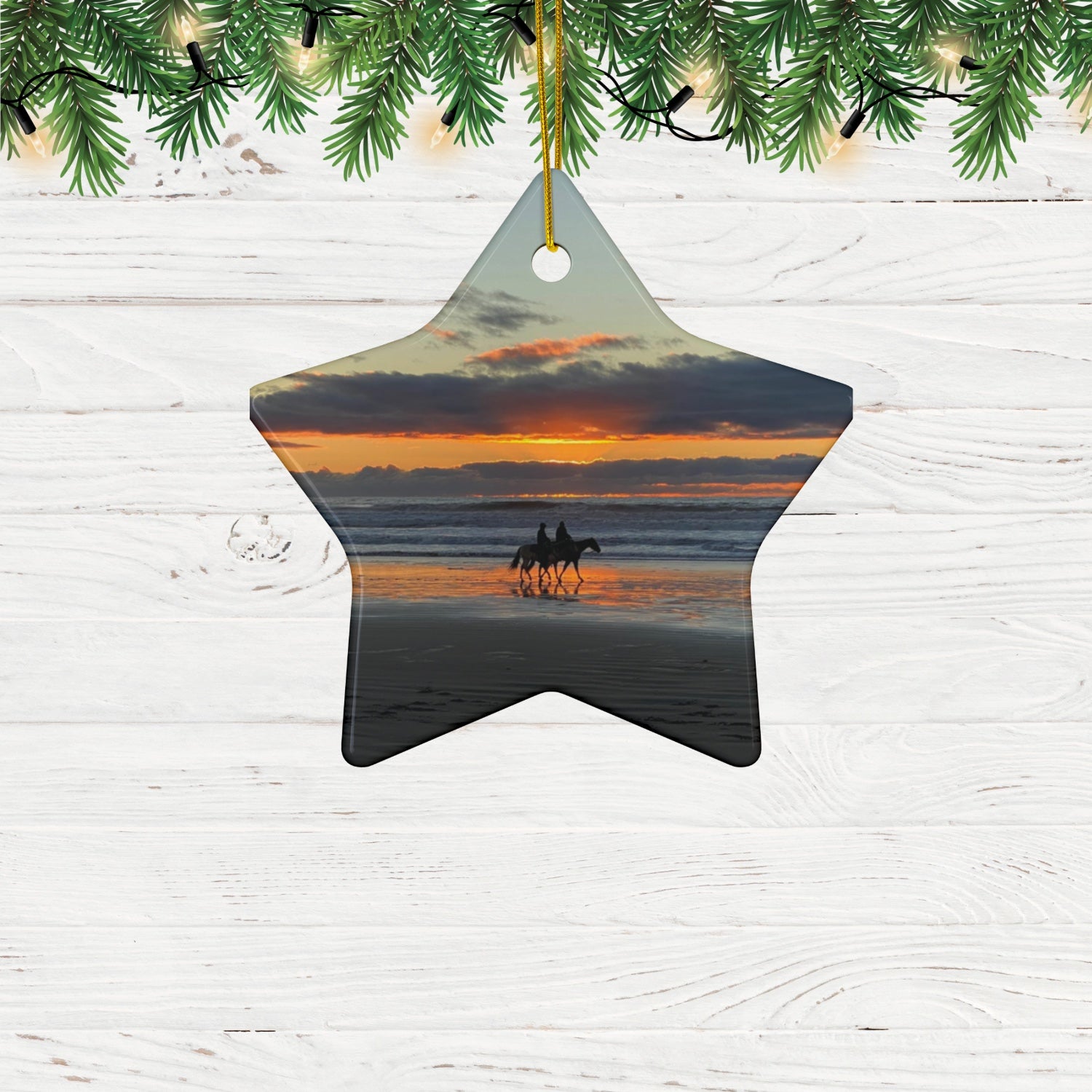 Star-shaped ceramic holiday ornament featuring a photograph of two horseback riders silhouetted on a beach at sunset with reflections in the wet sand, hanging from Christmas tree.