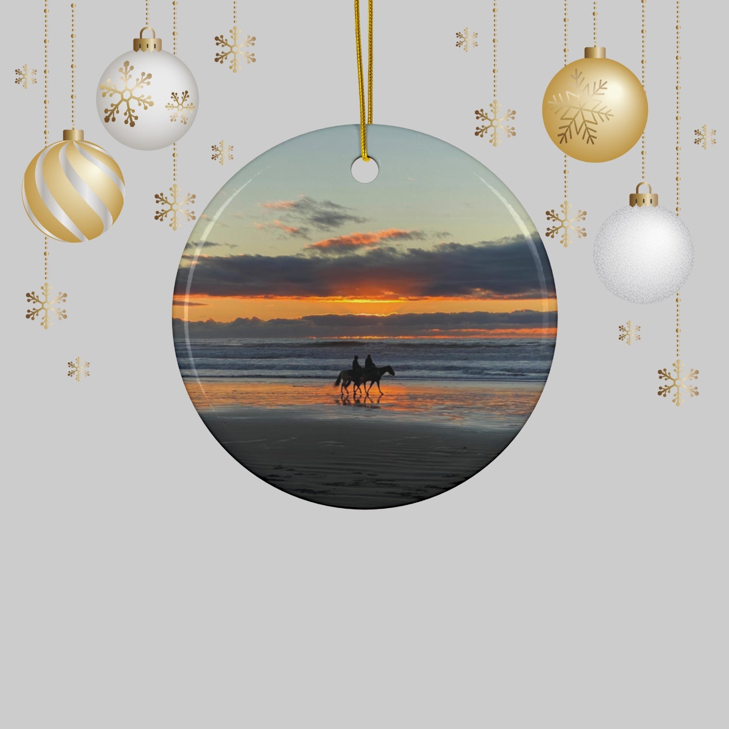 Ceramic holiday ornament featuring a photograph of two horseback riders silhouetted on a beach at sunset with reflections in the wet sand, surrounded by Christmas ornaments.