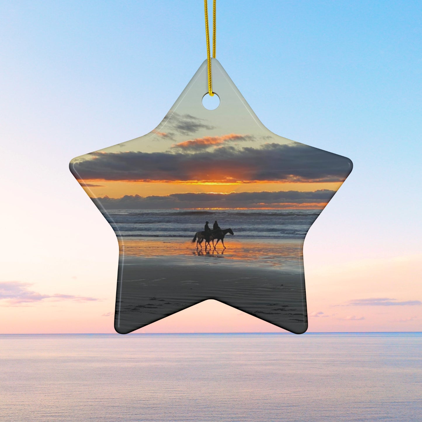 Star-shaped ceramic holiday ornament featuring a photograph of two horseback riders silhouetted on a beach at sunset with reflections in the wet sand.