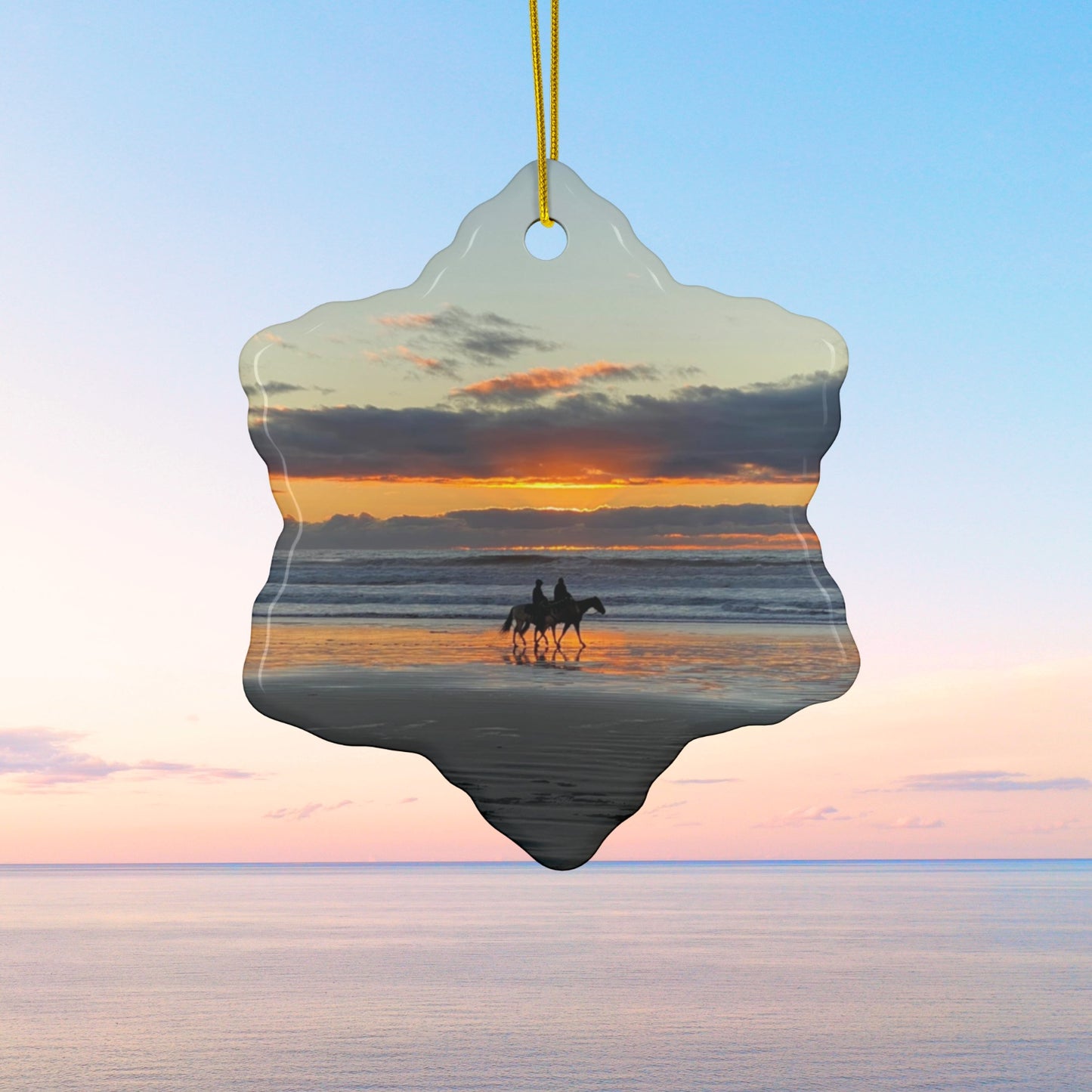 Ceramic holiday ornament featuring a photograph of two horseback riders silhouetted on a beach at sunset with reflections in the wet sand.
