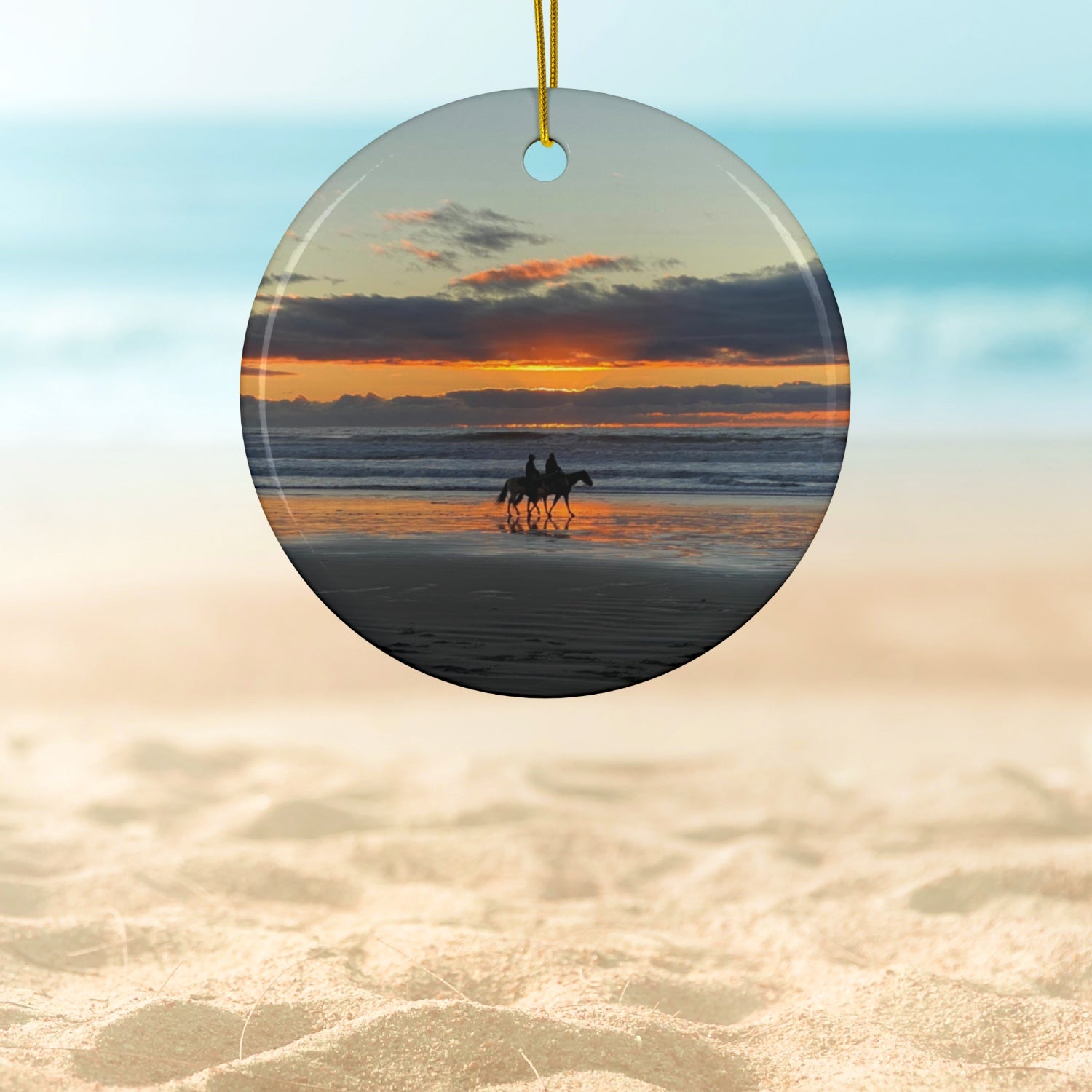 Ceramic holiday ornament featuring a photograph of two horseback riders silhouetted on a beach at sunset with reflections in the wet sand.
