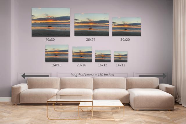 Canvas prints of two horseback riders on the beach at sunset above a sofa with measurements indicated.
