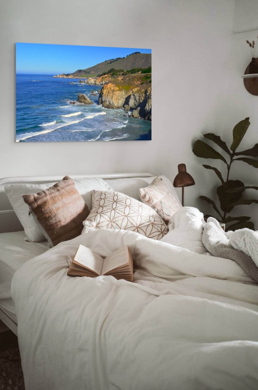Bedroom with a large canvas print of the rugged coastline in Big Sur, California, pillows, and a book.