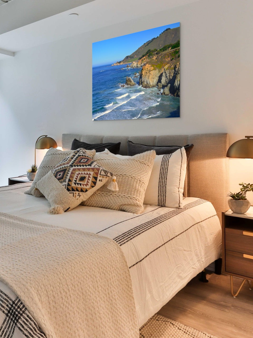 Bedroom with a large bed and decorative pillows, featuring a canvas print of the rugged coastline in Big Sur, California.