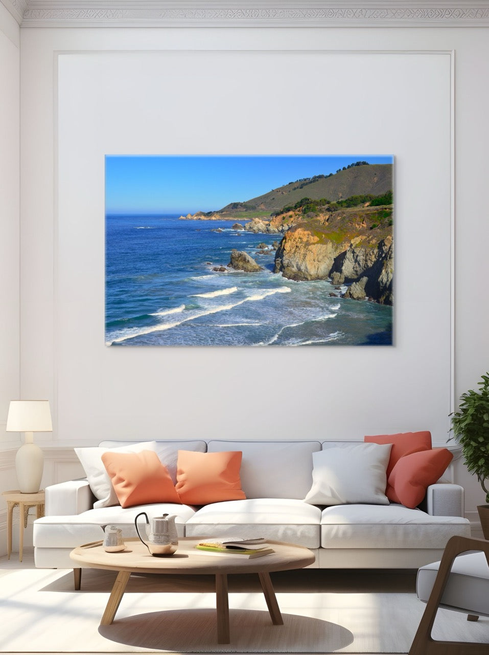 Living room with a large canvas print of the rugged coastline in Big Sur, California on the wall above a white sofa with orange and white cushions.