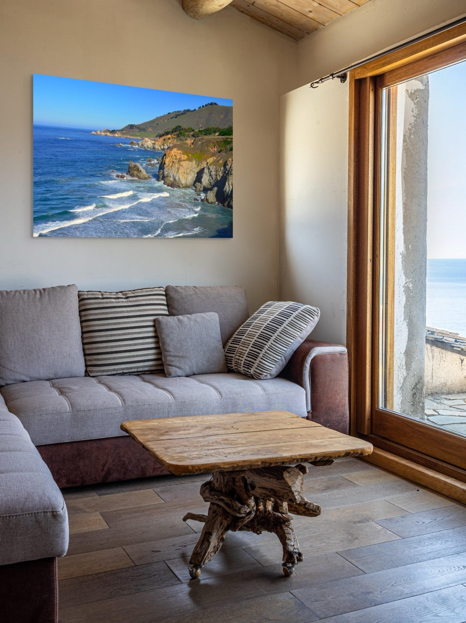 Living room with a gray sofa, wooden coffee table, and a large canvas print of the rugged coastline in Big Sur, California on the wall.