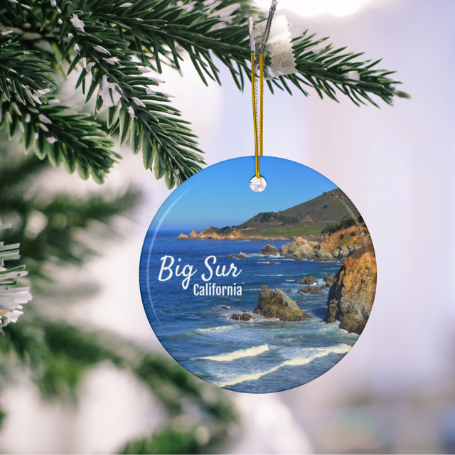 Ceramic Christmas ornament featuring a photograph of the rugged cliffs and deep blue Pacific Ocean along the Big Sur coastline in California hanging on a Christmas tree branch.