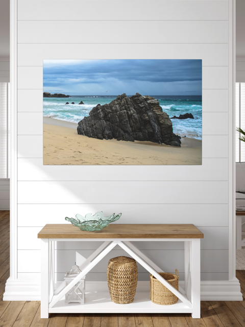 Big Sur California coastal rock formation canvas print on a wall above a wooden bench with storage baskets.