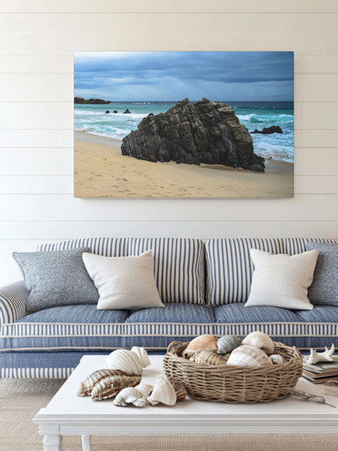 Big Sur California coastal rock formation canvas print above a striped sofa with decorative items on a coffee table.