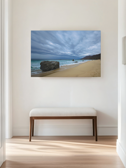 Canvas print of a Big Sur beach with a stormy sky on a wall above a bench in a room.