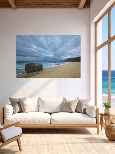 Living room with a canvas print of a Big Sur beach with a stormy sky on the wall, white sofa, and wooden floor.