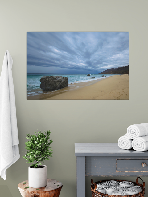 Canvas Print of a Big Sur beach with a stormy sky on a wall above a table with a plant and folded towels.