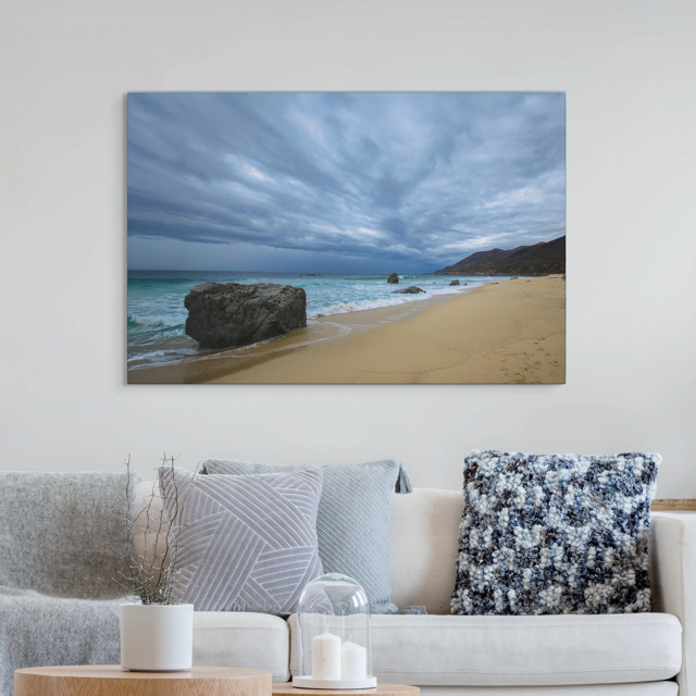 Canvas Print of a Big Sur beach with a stormy sky on a wall above a sofa with decorative pillows.