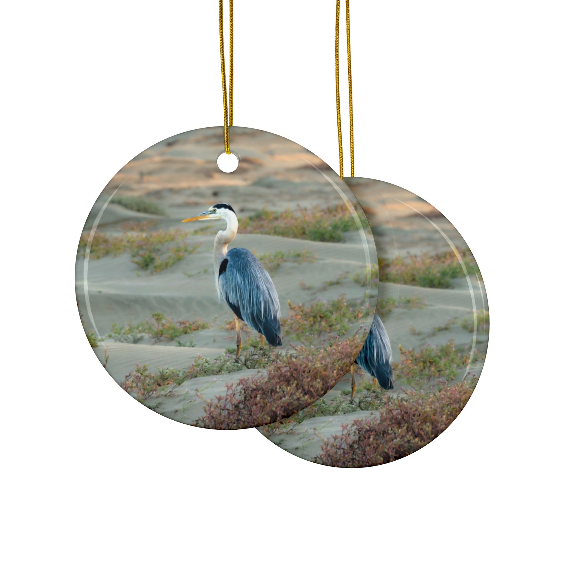Front and back side of a ceramic holiday ornament featuring a professional photograph of a Great Blue Heron standing among coastal reeds along the Pacific shoreline.