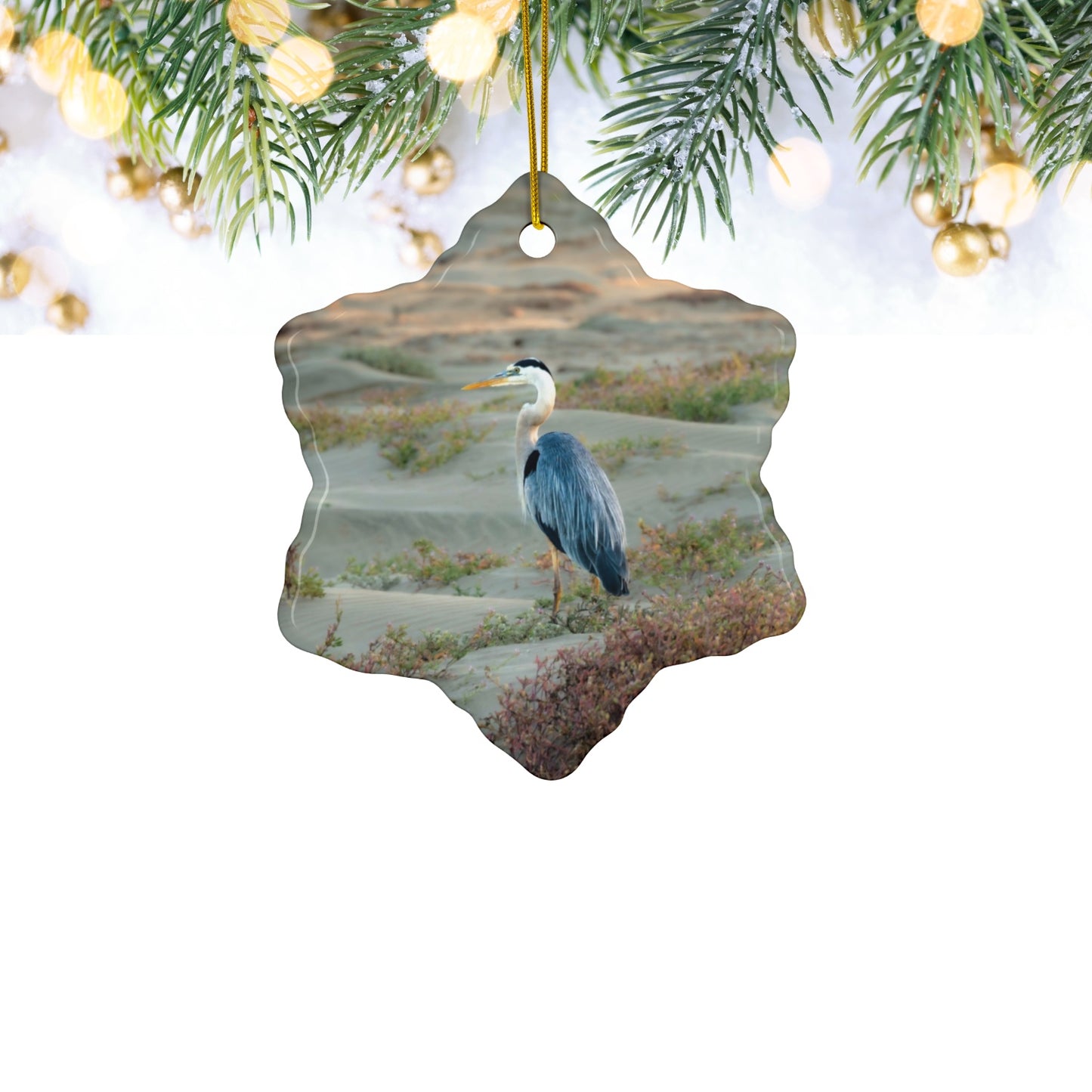 Ceramic holiday ornament featuring a professional photograph of a Great Blue Heron standing among coastal reeds along the Pacific shoreline.
