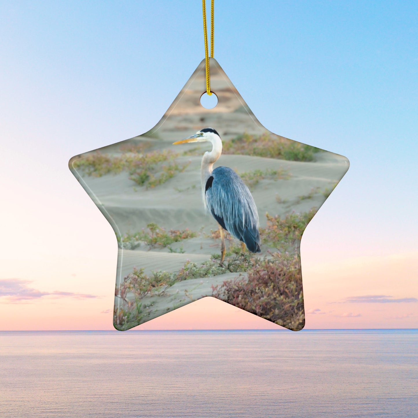 Star-shaped ceramic holiday ornament featuring a professional photograph of a Great Blue Heron standing among coastal reeds along the Pacific shoreline.