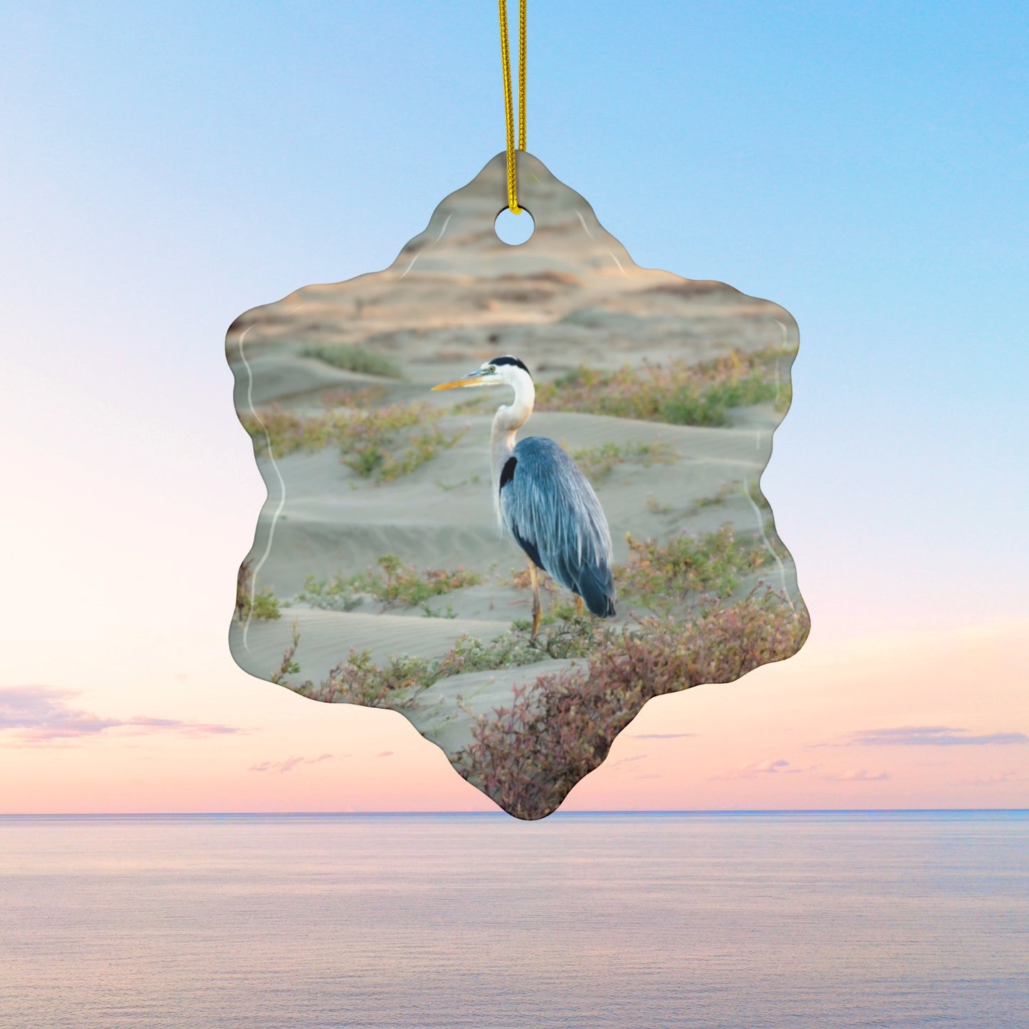 Ceramic holiday ornament featuring a professional photograph of a Great Blue Heron standing among coastal reeds along the Pacific shoreline.