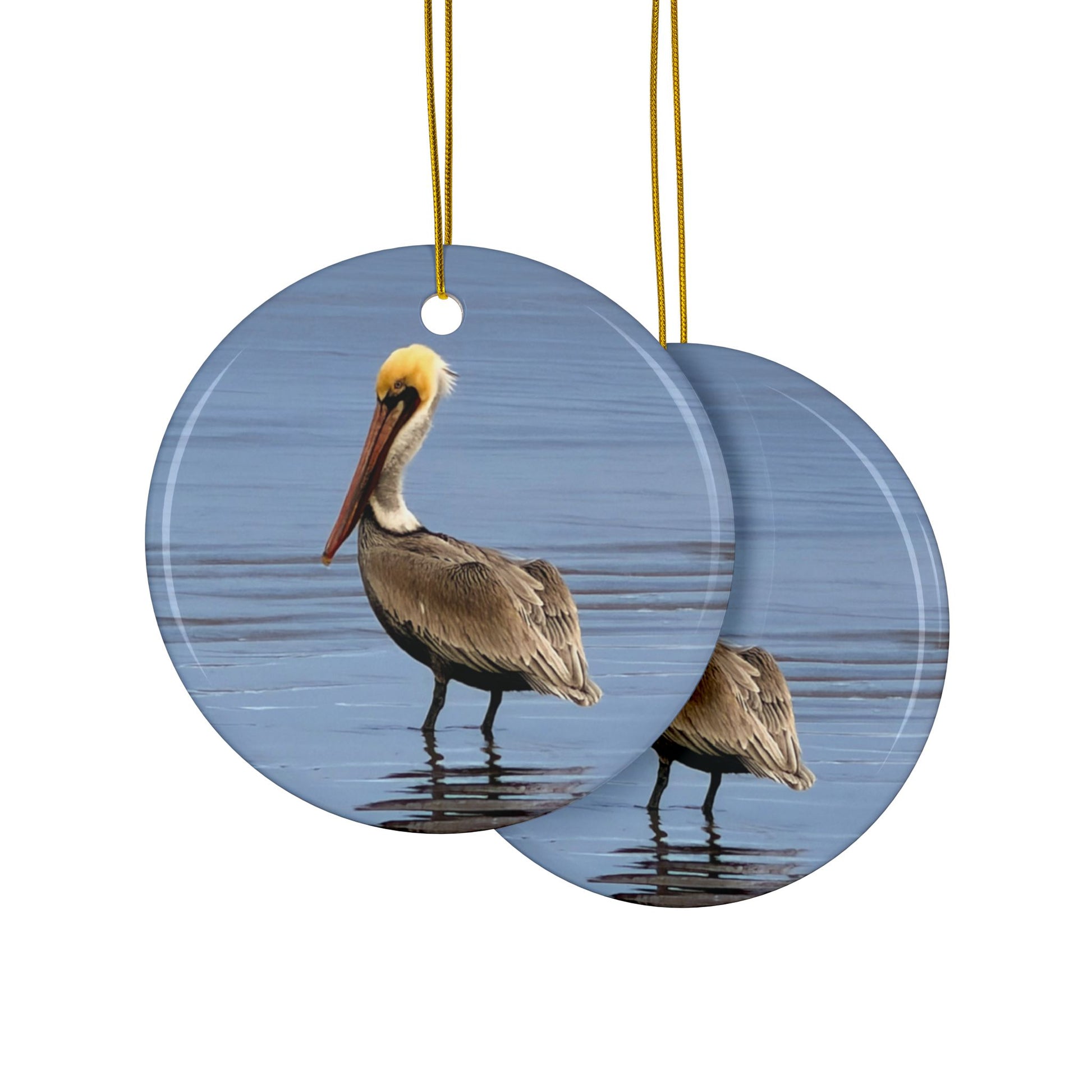 Front and back side of a ceramic holiday ornament featuring a professional photograph of a Brown Pelican standing on the shoreline.
