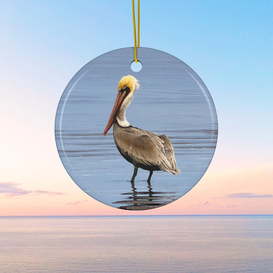 Ceramic holiday ornament featuring a professional photograph of a Brown Pelican standing on the shoreline.