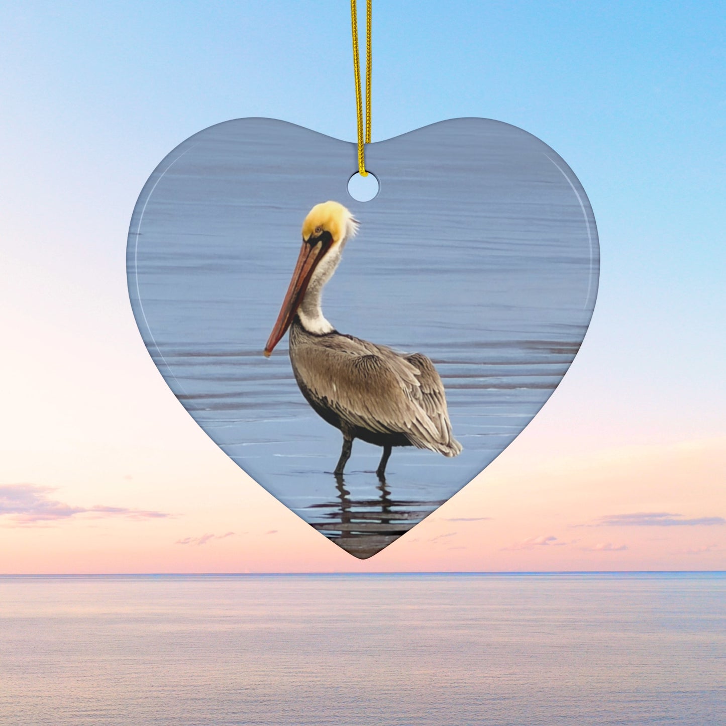 Heart-shaped ceramic holiday ornament featuring a professional photograph of a Brown Pelican standing on the shoreline.