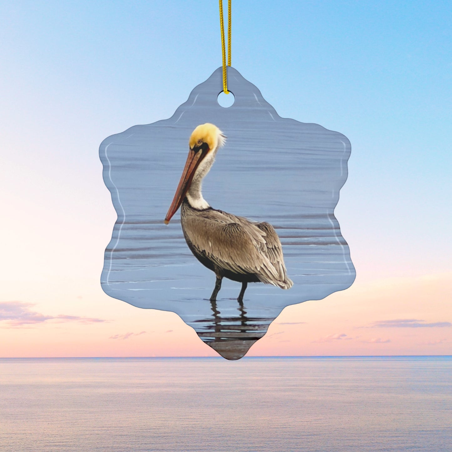 Ceramic holiday ornament featuring a professional photograph of a Brown Pelican standing on the shoreline.