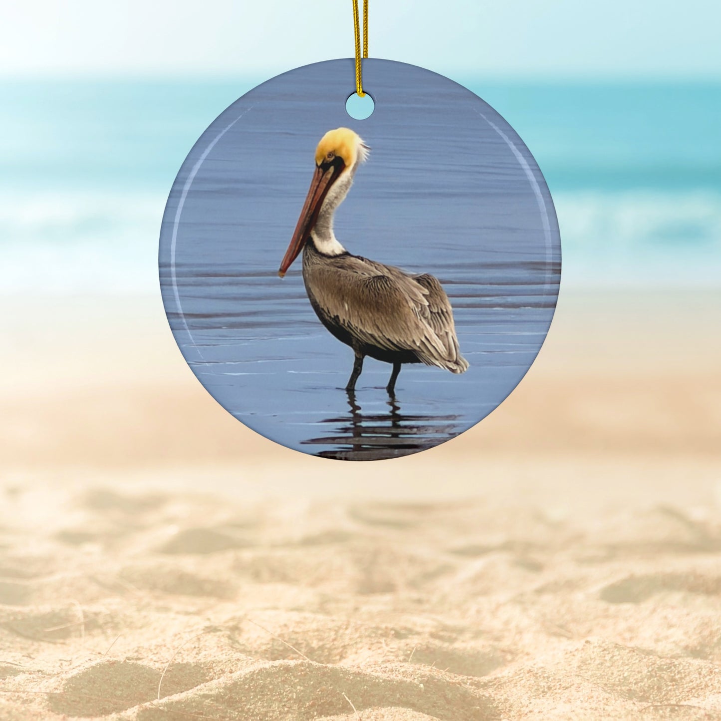 Ceramic holiday ornament featuring a professional photograph of a Brown Pelican standing on the shoreline.