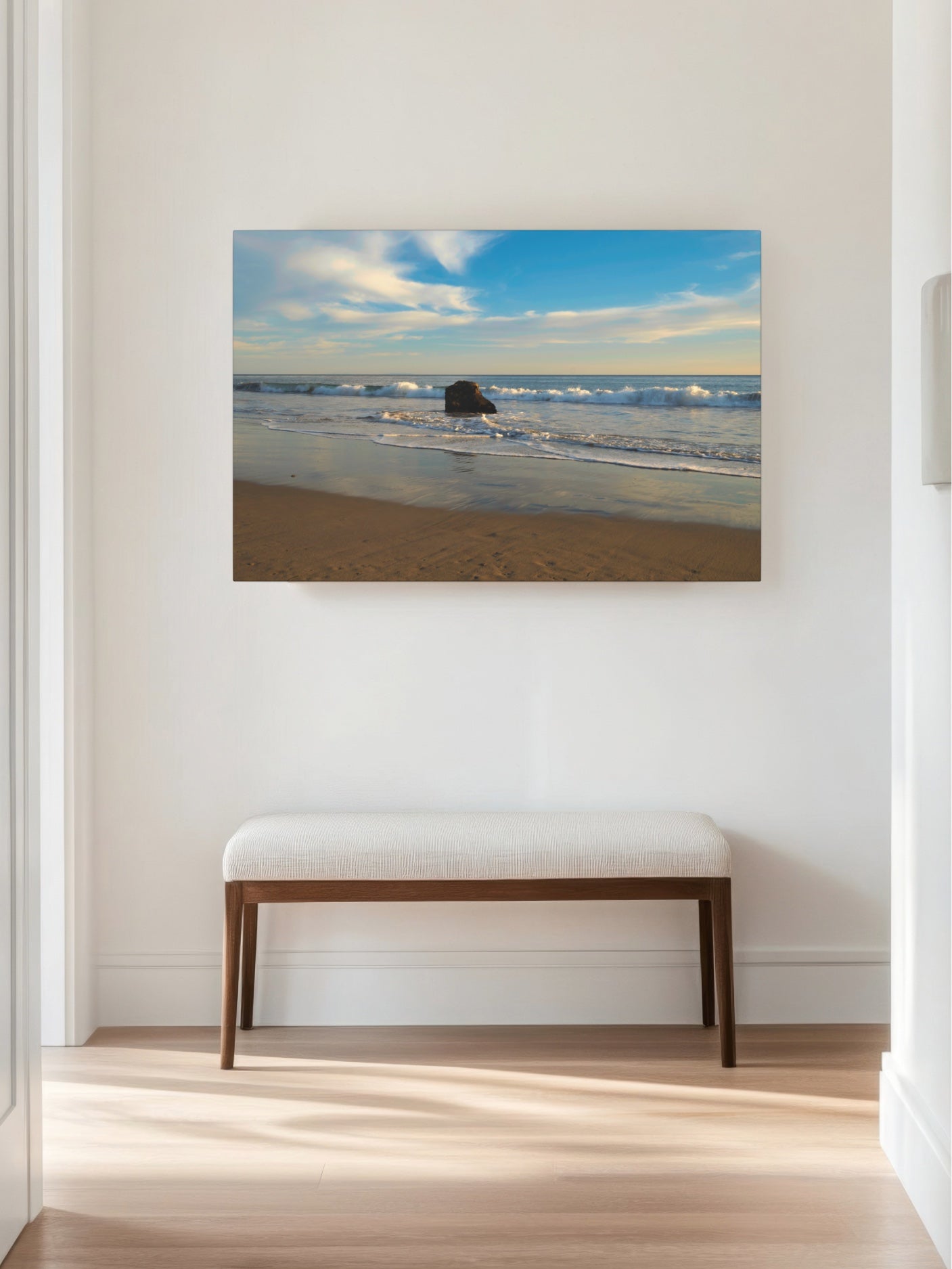Solitary rock on a California beach with ocean wave foam and sky reflection canvas print on a wall above a bench in a room.