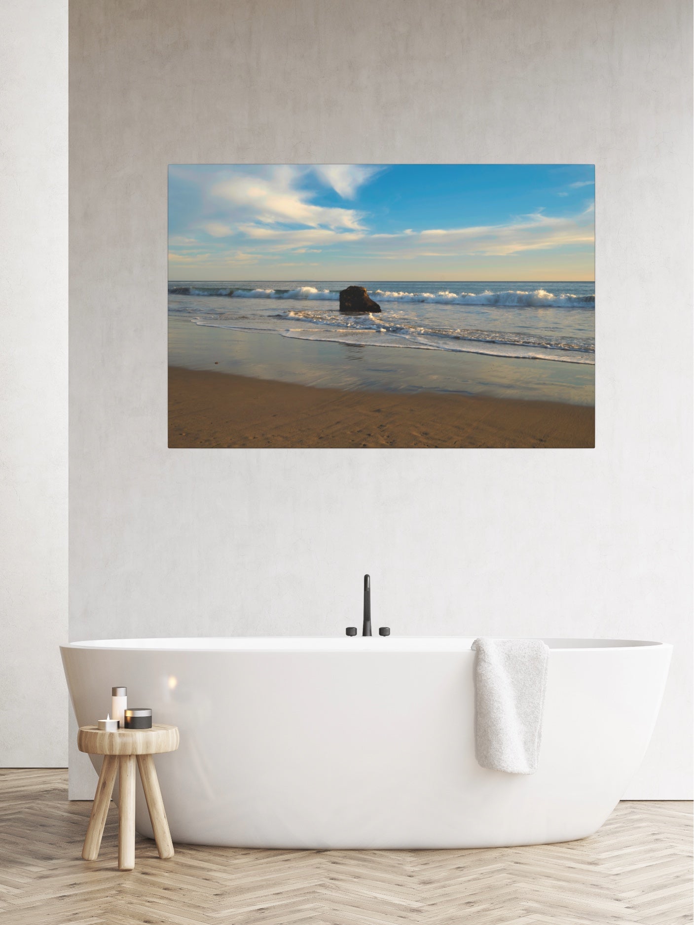 Solitary rock on a California beach with ocean wave foam and sky reflection canvas print on a wall above a white freestanding bathtub.
