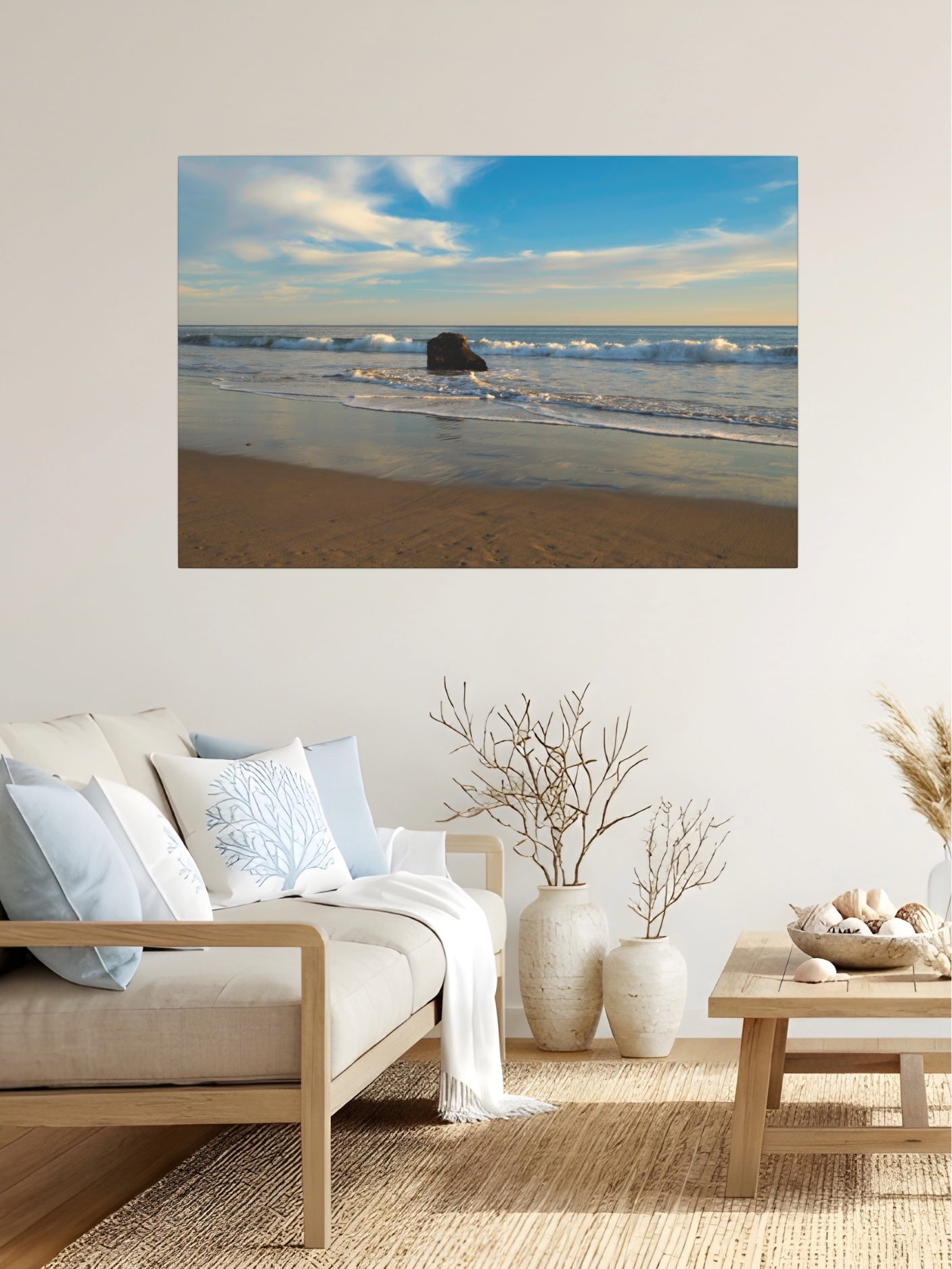 Solitary rock on a California beach with ocean wave foam and sky reflection canvas print on a wall above a living room with a sofa and decor.