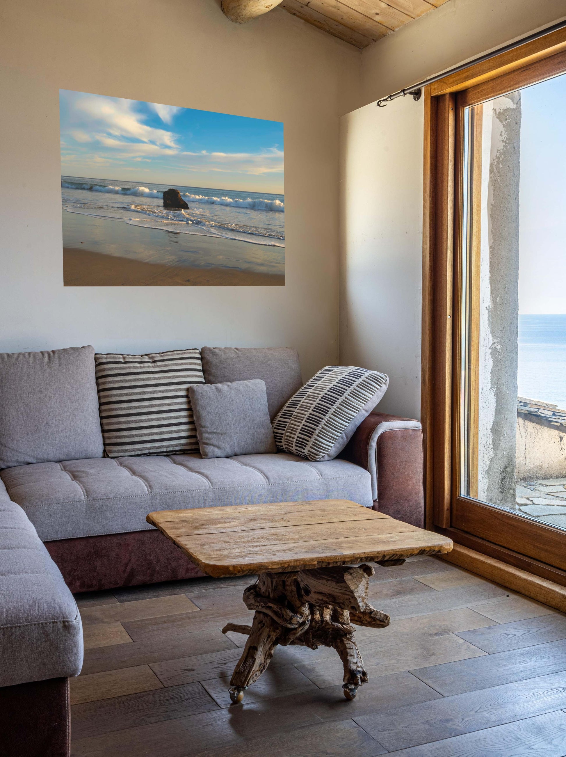 Living room with a gray sofa, wooden coffee table, and a solitary rock on a California beach with ocean wave foam and sky reflection canvas print.