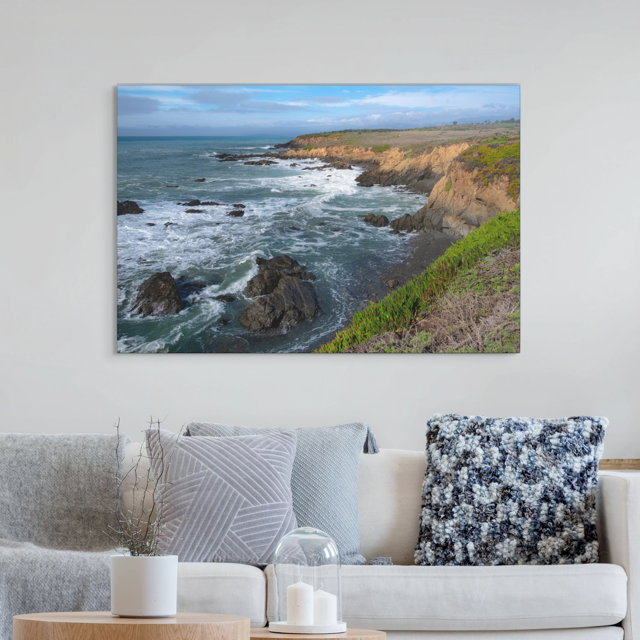 Canvas print of a coastal landscape hanging above a living room sofa.