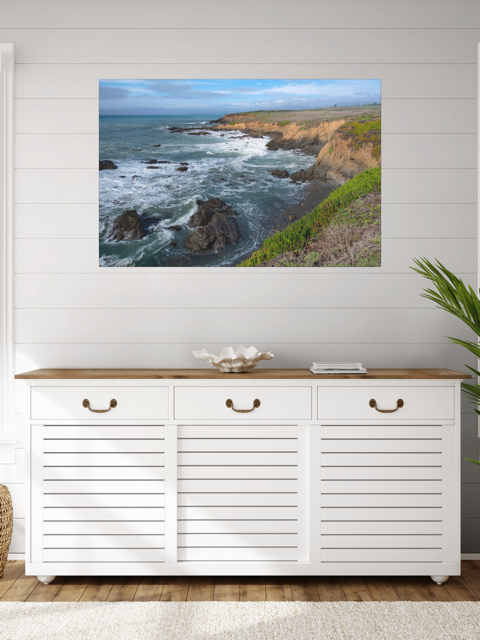 White sideboard with wooden top against a wall with a scenic ocean view canvas print.