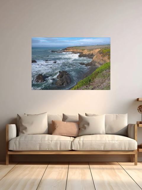 Coastal landscape print on a wall above a sofa with cushions.