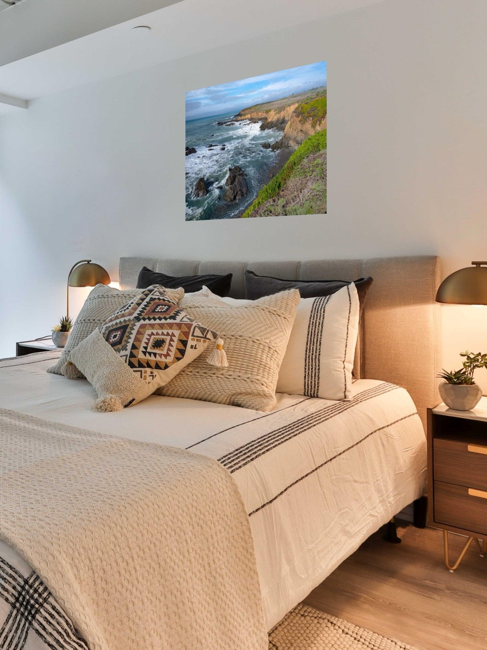Bedroom with a large bed and decorative pillows, featuring a scenic wall art of a coastal landscape.