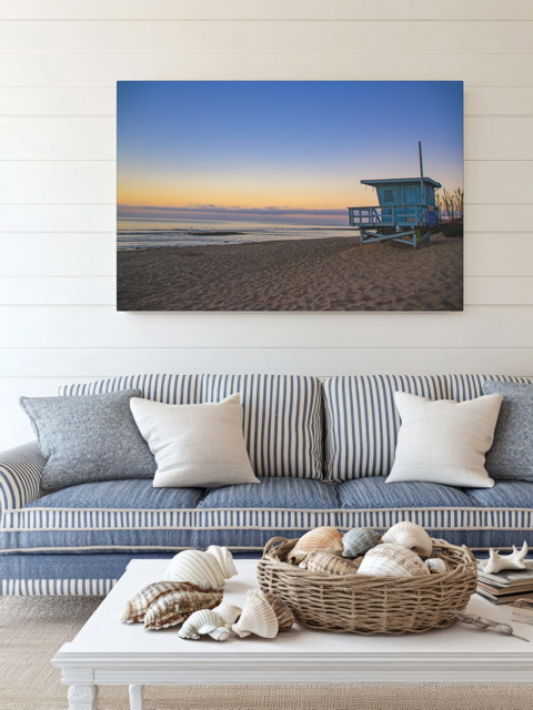 Canvas print of a California lifeguard tower at sunrise on a wall above a striped sofa.
