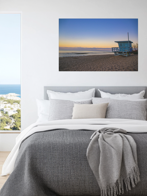 Bedroom with a canvas print of a California lifeguard tower at sunrise above the bed.